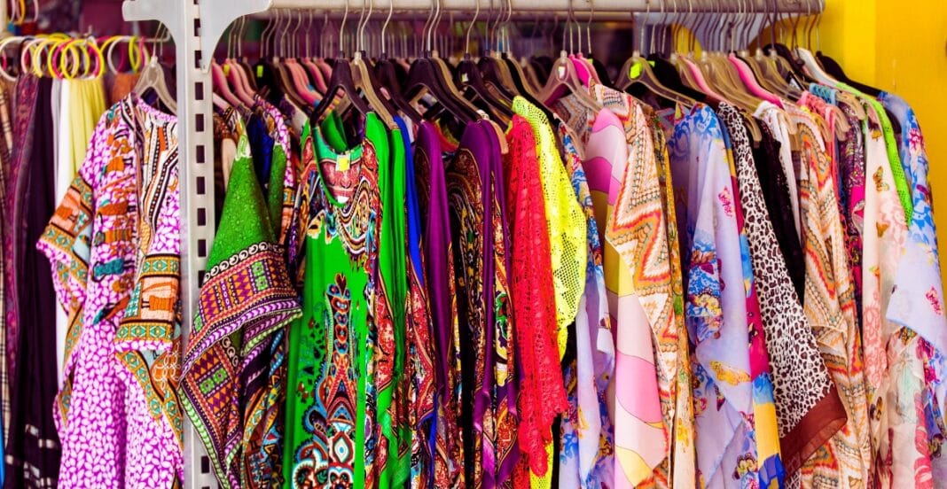 A rack of brightly colored, patterned dresses hanging on hangers in a clothing store.