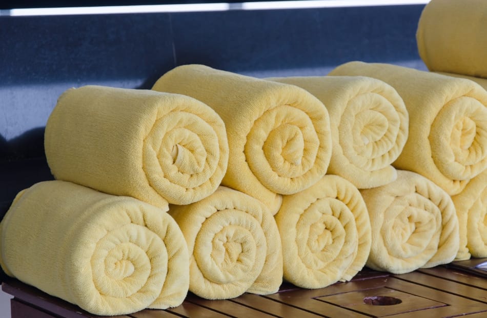 A neatly stacked row of soft, yellow rolled towels arranged on a wooden surface.