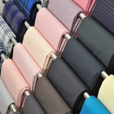 A display of polyester fabric rolls in various colors and patterns, including stripes and solids, arranged on a rack.