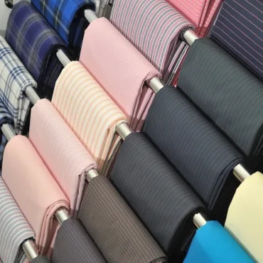 A display of polyester fabric rolls in various colors and patterns, including stripes and solids, arranged on a rack.
