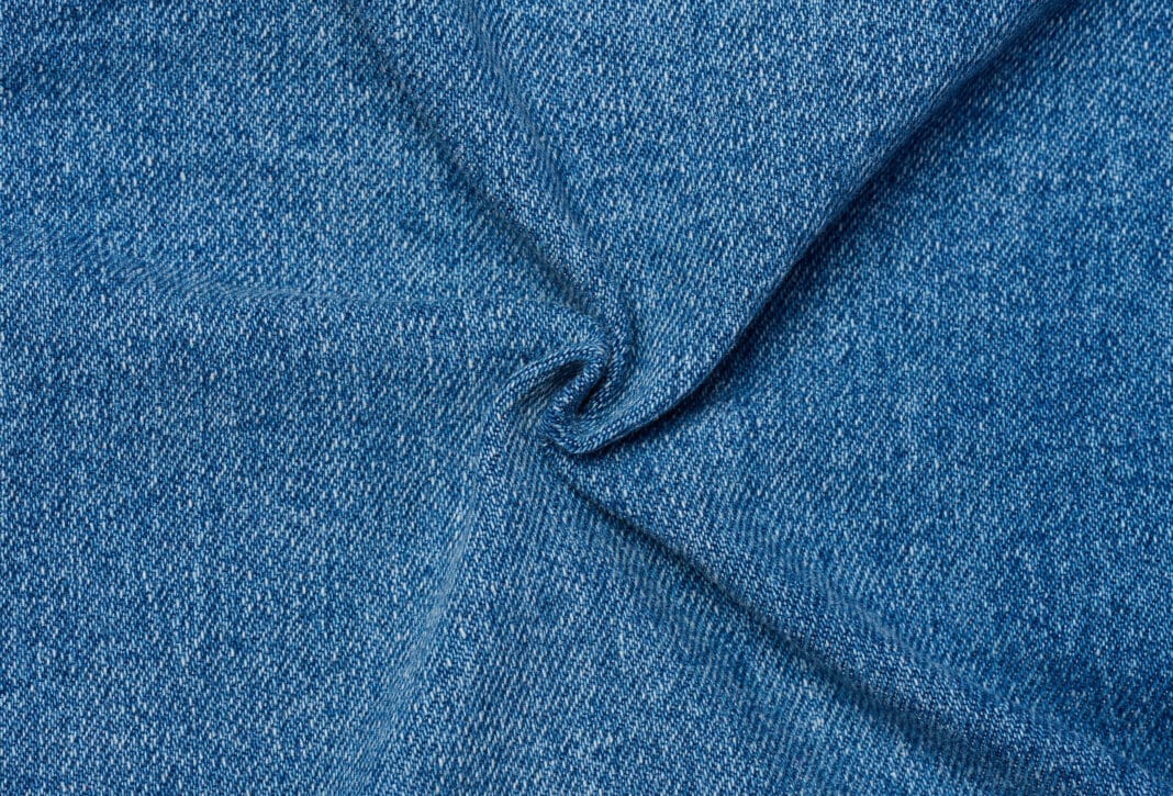 Close-up image of blue denim cotton fabric with visible weave texture and slight folds.