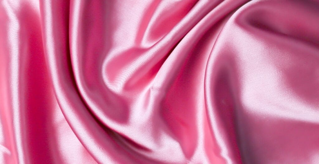 Close-up image of pink, shiny, and smooth breathable polyester fabric with gentle folds.
