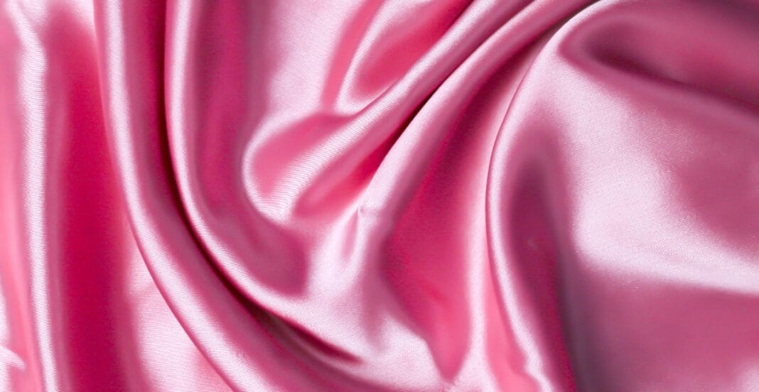 Close-up image of pink, shiny, and smooth breathable polyester fabric with gentle folds.