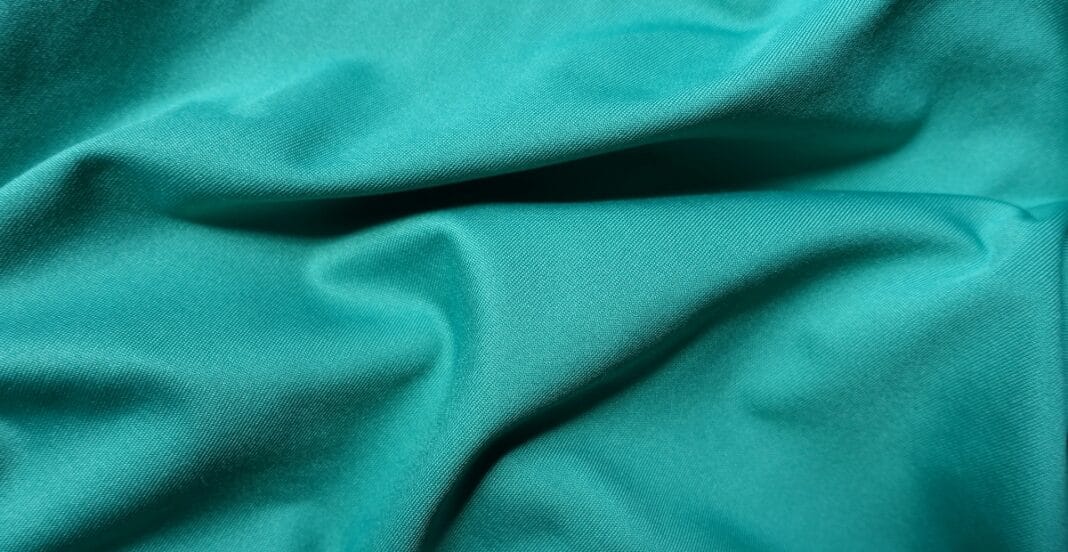 Close-up image of teal brushed polyester fabric, showcasing a smooth and slightly textured surface suitable for casual wear.