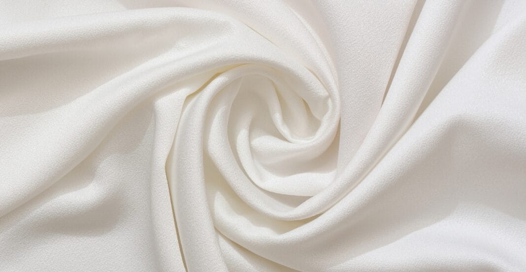 A close-up image of smooth, pure white cotton fabric with soft folds and gentle draping.