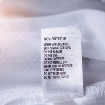 Clothing care label on a white polyester garment, displaying washing instructions.