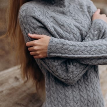 A person wearing a gray cable-knit sweater, with arms crossed over their chest.