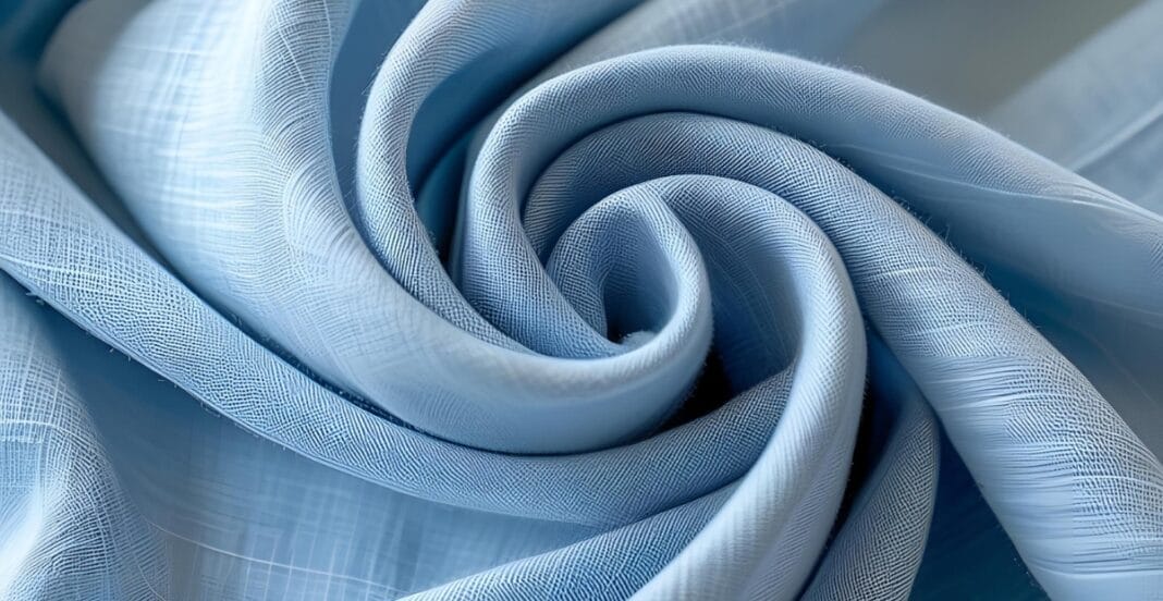A close-up of light blue chambray fabric, intricately rolled into a spiral, showcasing its woven texture and soft sheen.