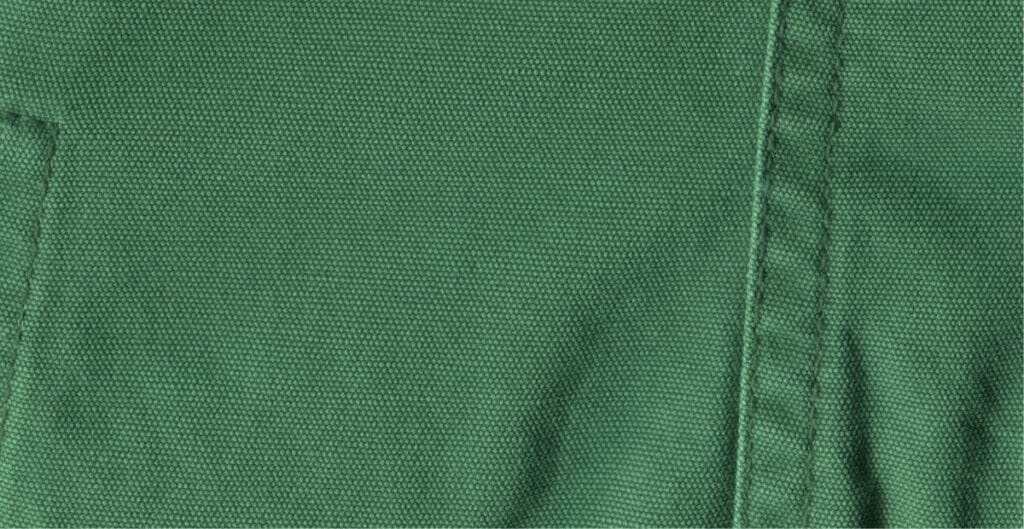 Close-up image of green cotton chambray fabric showing its tightly woven texture and faint diagonal weave pattern.