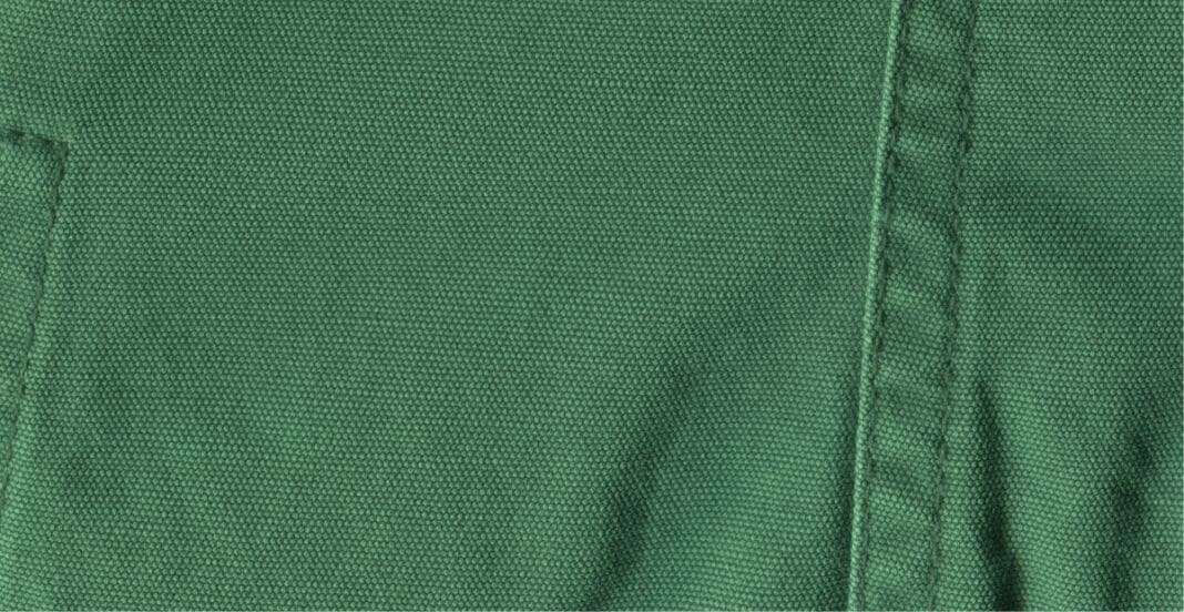 Close-up image of green cotton chambray fabric showing its tightly woven texture and faint diagonal weave pattern.