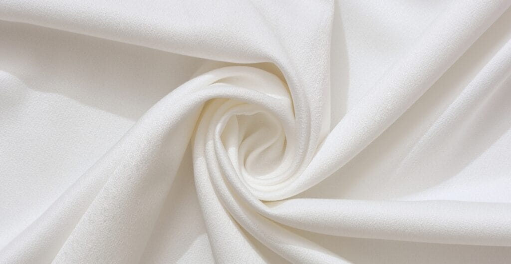 A close-up of smooth, white cotton fabric gently twisted to form a spiral pattern.