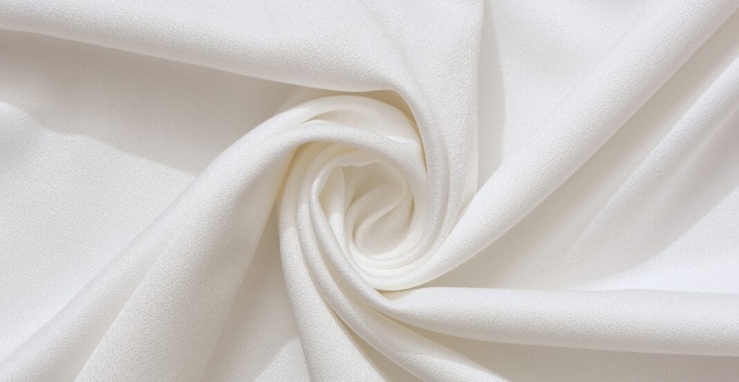 A close-up of smooth, white cotton fabric gently twisted to form a spiral pattern.