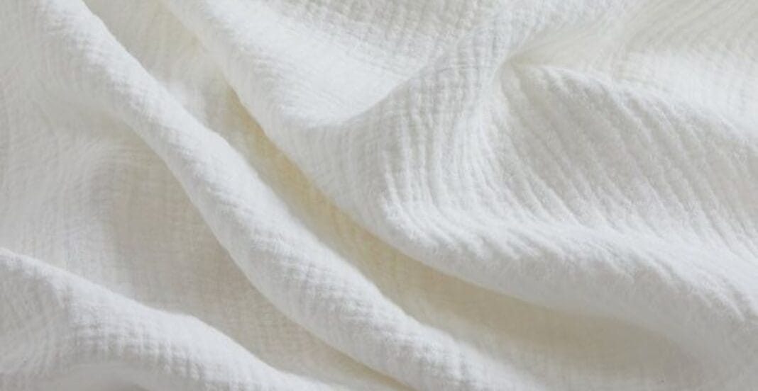 Close-up image of soft, white cotton muslin fabric, showing gentle folds and a textured weave.