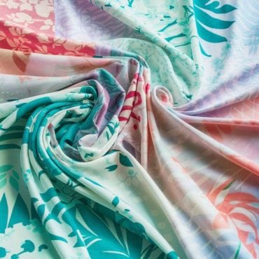 Colorful, lightweight fabric with a tropical floral pattern, gently draped in soft folds, suitable for summer clothing.