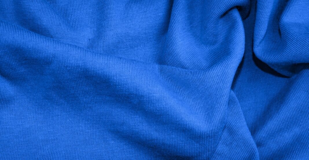 Close-up image of blue fabric with visible weave texture and folds, made from a cotton-polyester blend.