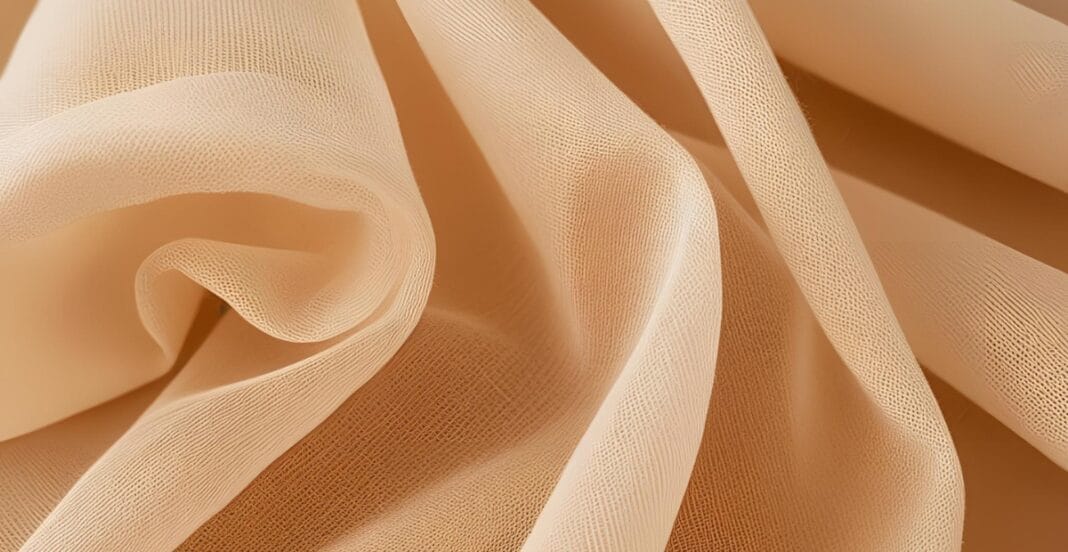 Close-up image of soft, peach-colored cotton voile fabric with smooth, gentle folds.