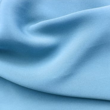 A close-up of light blue chambray fabric with soft folds and smooth texture.