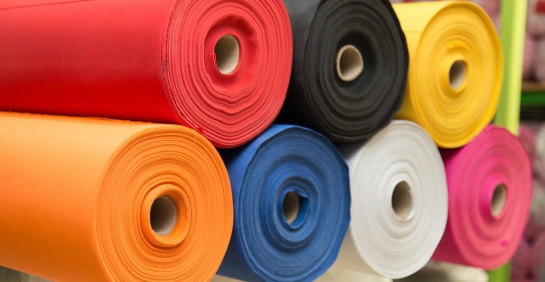 Close-up of colorful rolls of fabric in red, black, yellow, orange, blue, white, and pink, stacked horizontally.
