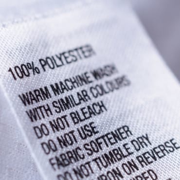 Close-up of a care label on a white fabric with washing instructions, mentioning polyester.