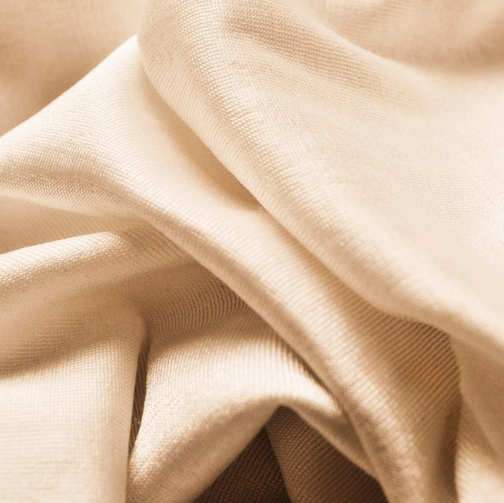 Close-up photo of light beige, smooth, and slightly shiny cotton fabric draped softly, with visible fine weave and texture.
