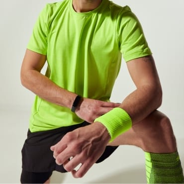 Man dressed in bright green loose-fitting polyester sportswear, stretching outdoors.