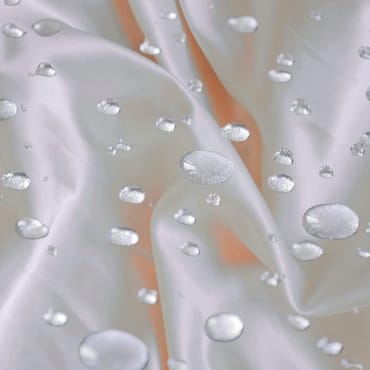 Close-up of a soft, smooth microfiber fabric with water droplets on its surface, highlighting its waterproof and polyester material.