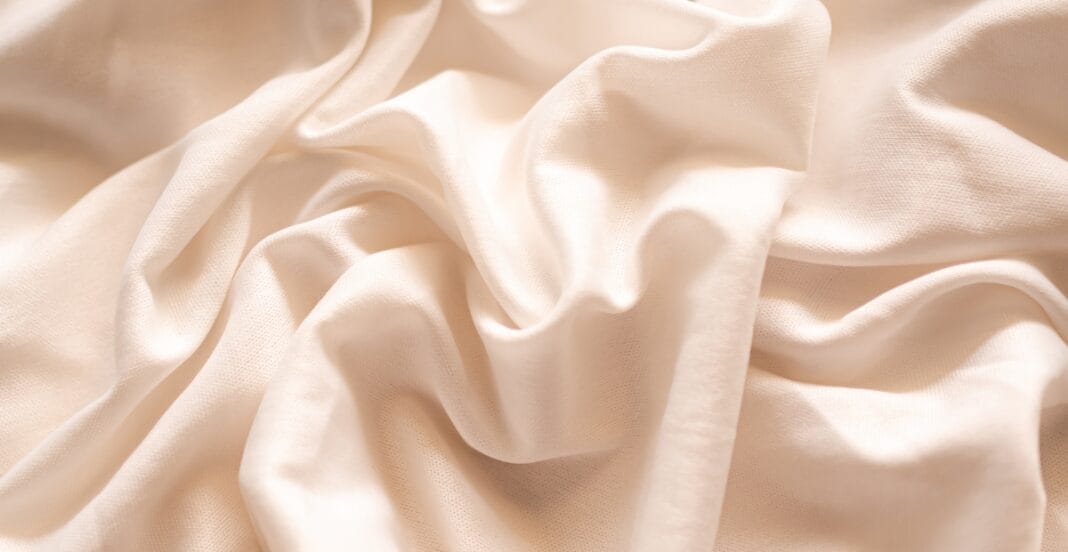 Close-up of soft, cream-colored organic cotton fabric with gentle folds and smooth texture.