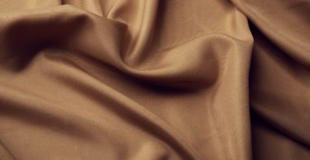 Close-up of a beige PET polyester fabric with soft folds and smooth texture.