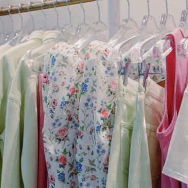 Clothes hanging on a rack, including floral, pastel, and pink garments, showcasing various fabrics, possibly including polyester.