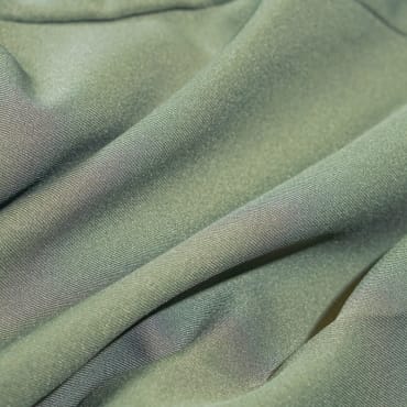 Close-up of light green polyester fabric with a smooth texture, showing gentle folds.