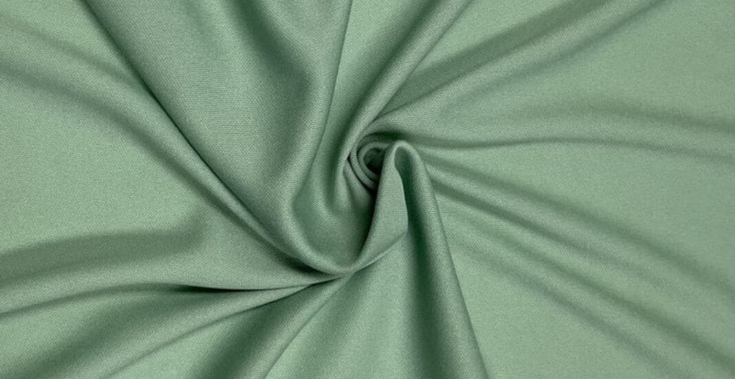 A piece of green polyester knit fabric arranged in a swirl pattern with soft folds.