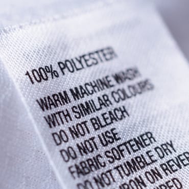 Clothing label with care instructions for 100% polyester, including washing, bleaching, and fabric softener guidelines.