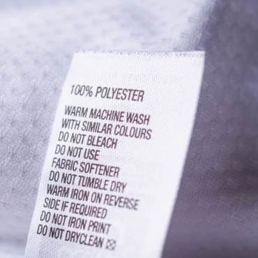 Clothing label indicating care instructions for 100% polyester fabric, including washing, drying, and ironing guidelines.