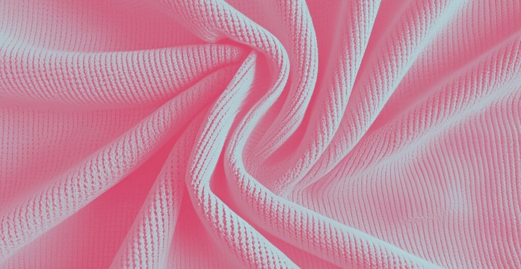 Close-up view of pink polyester pique knit fabric with textured, patterned surface and soft folds.