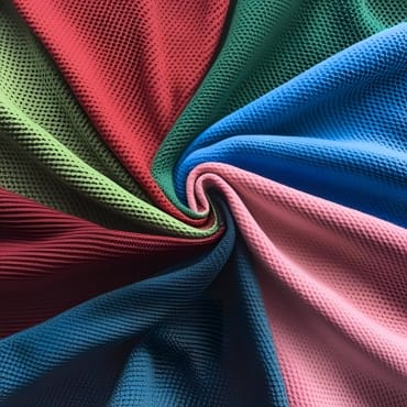 A close-up image of multi-colored polyester pique knit fabric, arranged in a swirl pattern.