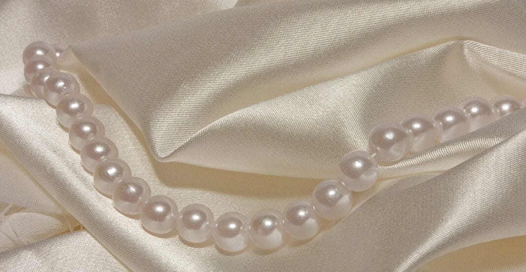 A pearl necklace resting on a smooth, satin-like fabric with a silky sheen and soft folds.