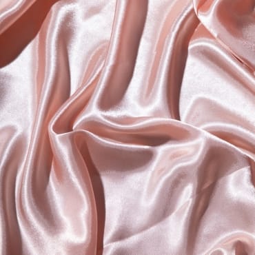 Close-up of soft, blush pink polyester silk blend fabric with smooth, flowing folds and a glossy finish.
