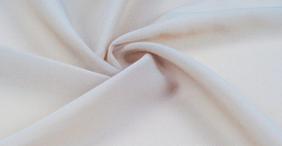 Close-up image of a soft, cream-colored polyester spandex blend fabric with a gentle drape and subtle texture.