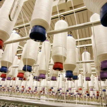 Multiple large spools of PET polyester yarn hanging in a textile manufacturing facility, arranged in rows.