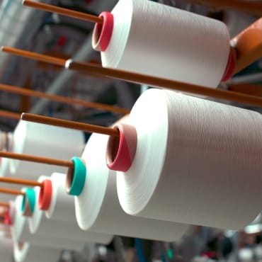 Close-up of large spools of PET polyester yarn mounted on an industrial reel, with the yarn appearing smooth and white.