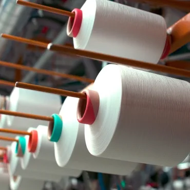 Close-up of large spools of PET polyester yarn mounted on an industrial reel, with the yarn appearing smooth and white.