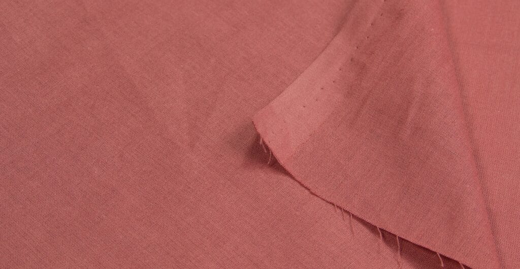 A close-up image of a pink poplin cotton fabric, showing the texture and weave of the material with a folded edge.