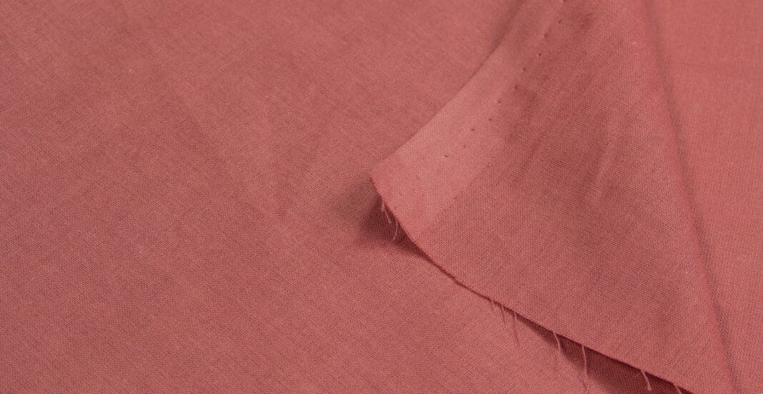 A close-up image of a pink poplin cotton fabric, showing the texture and weave of the material with a folded edge.