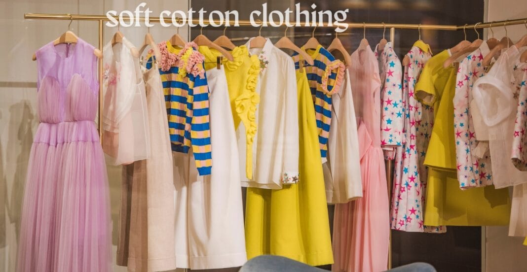 A display of colorful, soft cotton clothing on hangers in a store, featuring dresses, tops, and jackets in pastel and bright shades.