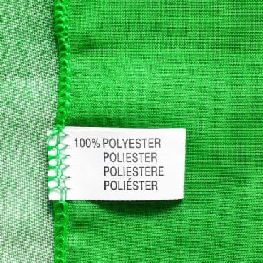 Close-up of a bright green polyester knit fabric with a stitching guide tag attached, showing the fabric's edge and seam detail.