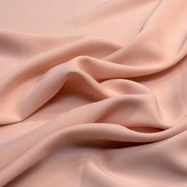 Soft, flowing fabric in a light peach color with gentle folds and smooth texture, showcasing a polyester-rayon blend.
