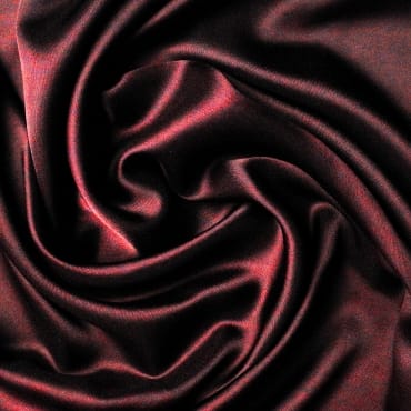 A close-up image of a dark, shiny, and smooth fabric with silk-like appearance, featuring swirling folds in a deep reddish-brown color.