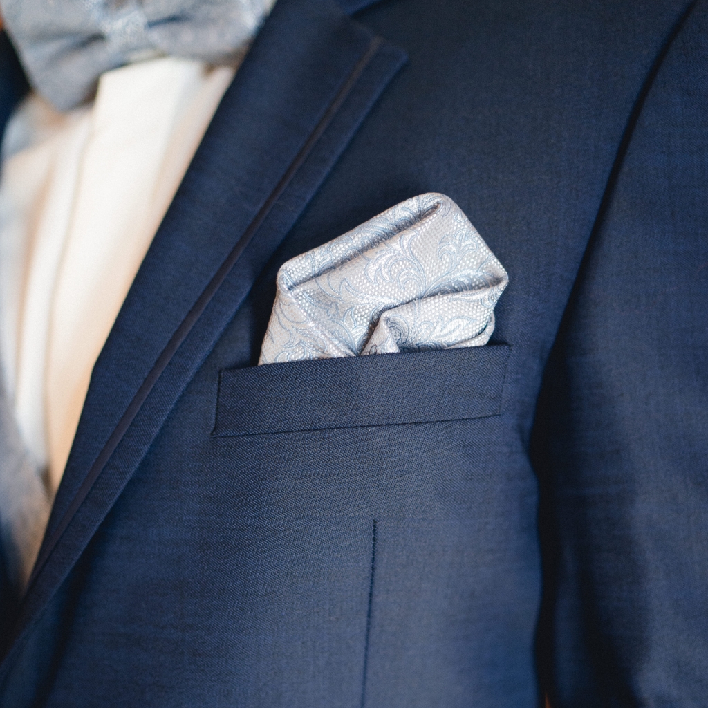 A silver pocket square with an intricate paisley pattern tucked neatly into the breast pocket of a dark blue suit jacket.