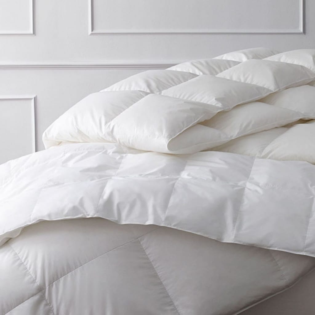 A close-up of a neatly made bed with white pillows and a white quilted comforter, set against a white paneled wall.
