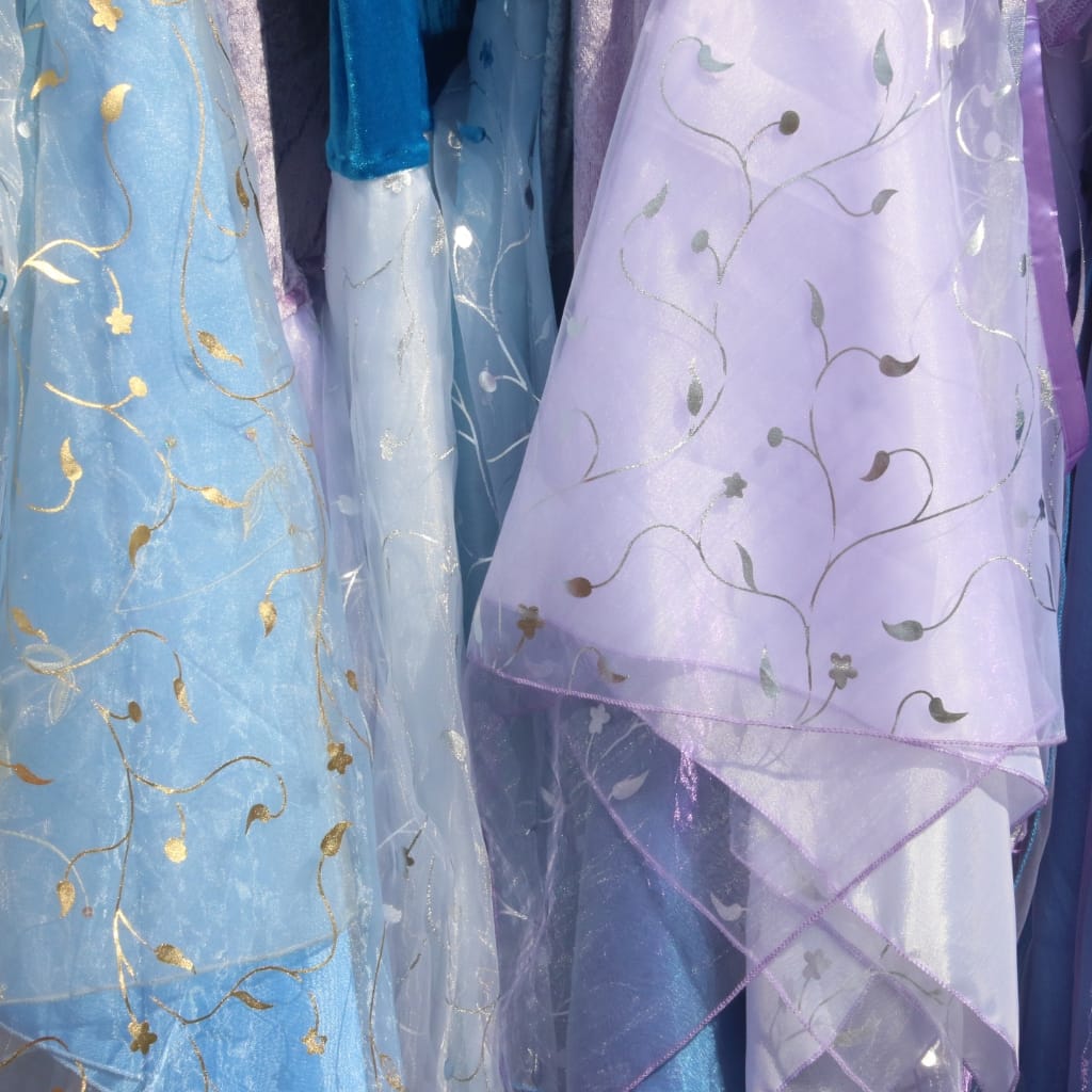 Close-up image of elegant, semi-transparent fabrics in pastel shades (light blue, lavender, and white) with gold embroidered floral and vine patterns. The fabrics have a delicate, flowy appearance, showing intricate embroidery and lightweight, soft drape qualities.